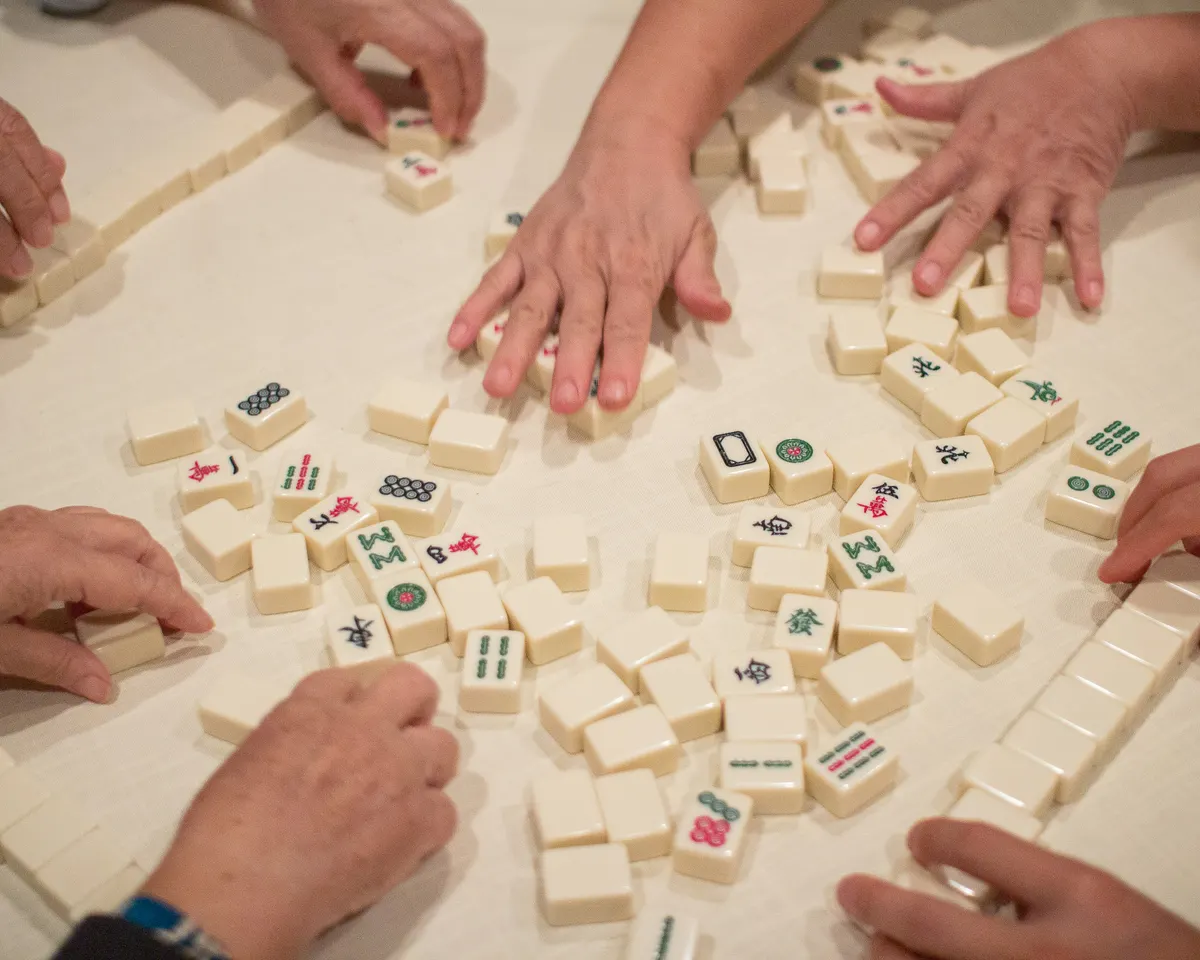 A player's hand arranging engraved Mahjong tiles on a rack during a game