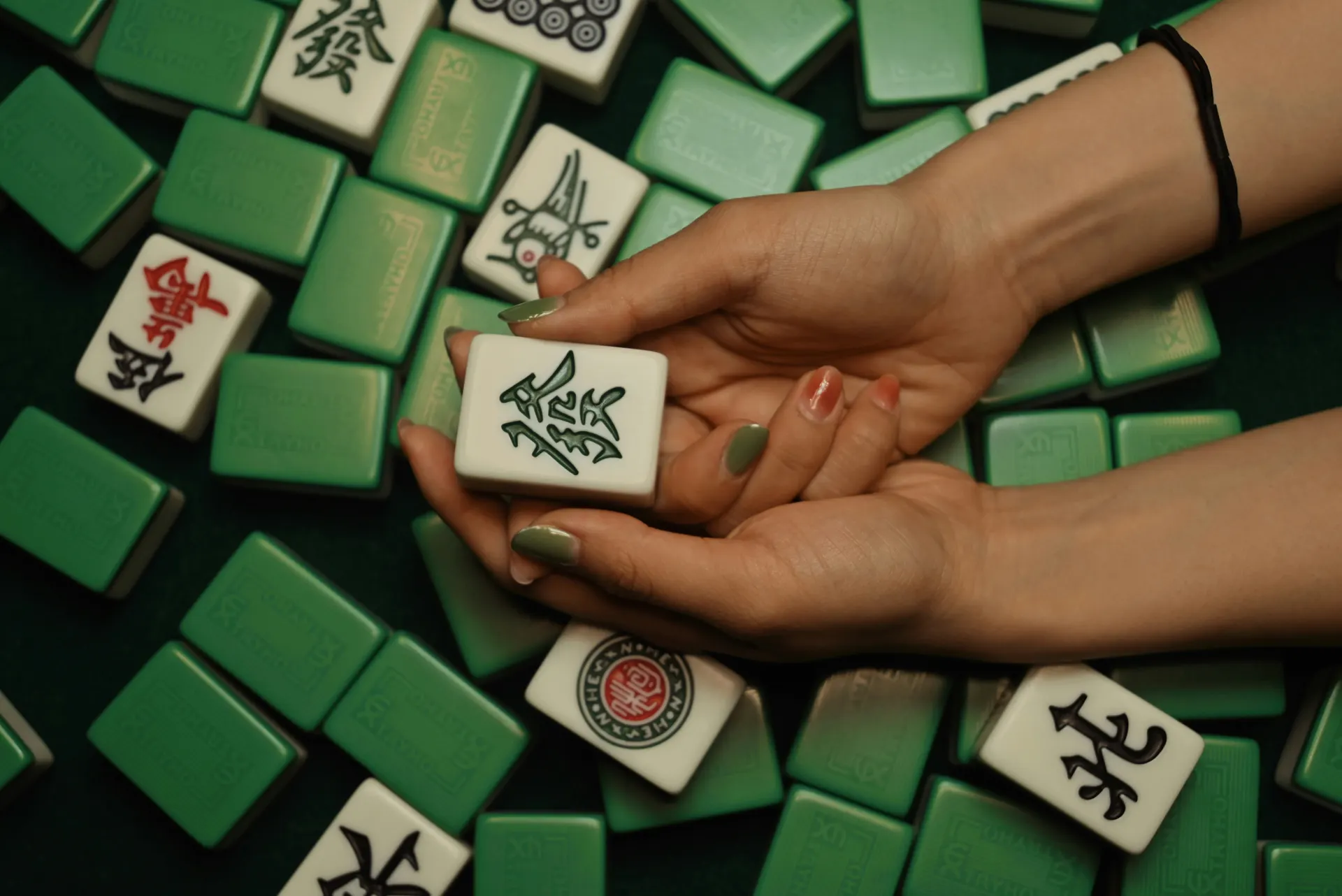 A player holding a hand of Mahjong tiles above a game in progress